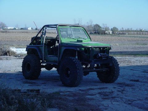 1992 Ford Bronco - Modified off-road vehicle with custom roll cage and oversized tires sits in a field.