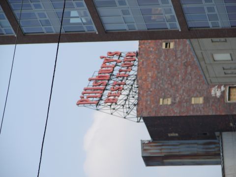 1992 Ford Taurus - A large red neon sign is visible on the side of a brick building, with a modern glass-paneled structure above.