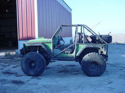 1992 Ford Bronco - Modified off-road vehicle with extensive roll cage and large tires sits outside a barn.
