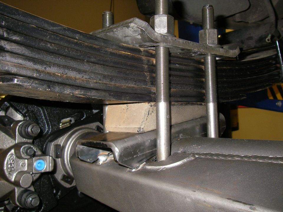 Close-up of vehicle leaf spring assembly with U-bolts and a block spacer