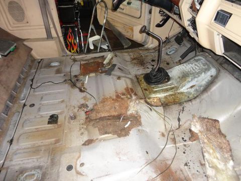 1981 Ford Bronco - The interior floor of the vehicle shows extensive rust damage and exposed wiring, with a manual transmission shifter visible.