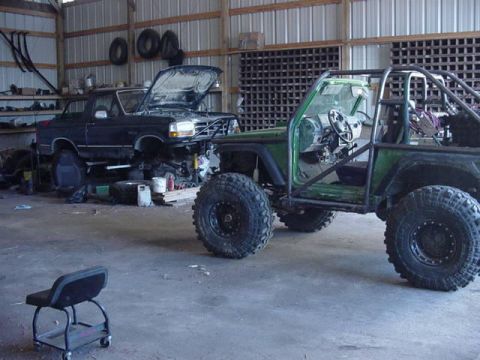 1992 Ford Bronco - Two vehicles, a black Ford Bronco and a green buggy, are parked inside a garage with various tools and parts around them.