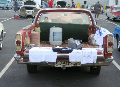 1976 Ford Ranchero - The bed of a red Ford Ranchero is filled with various items, including a large white barrel and old gas cans.