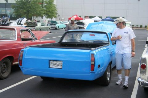 1976 Ford Ranchero - A blue pickup truck is parked next to a red vehicle, with a man standing nearby.