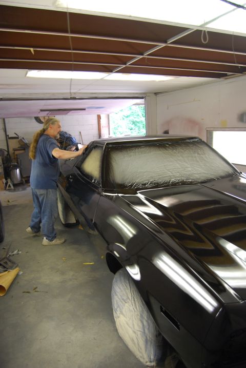 1975 Ford Ranchero - A person tapes off the windshield of a black 1975 Ford Ranchero inside a garage, likely preparing for paint.
