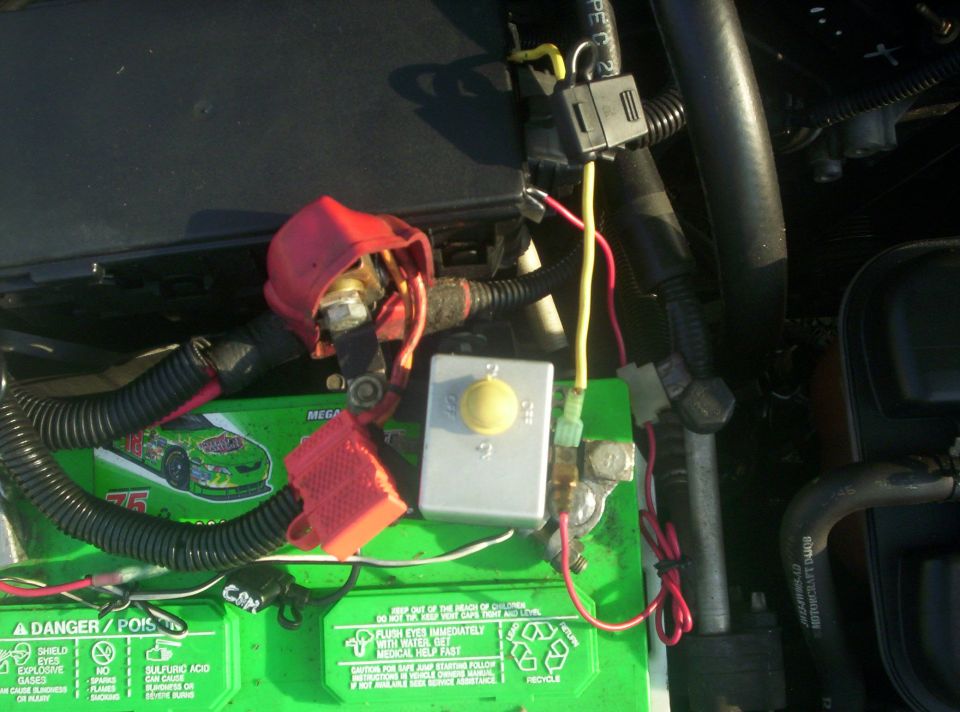 Green car battery with yellow-knob disconnect switch and added fused wiring in an engine bay