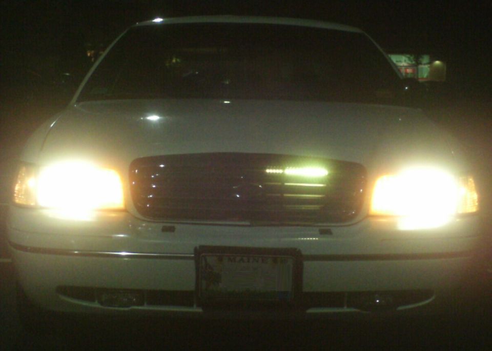 White 1998 Ford Crown Victoria front view at night, headlights on, license plate visible