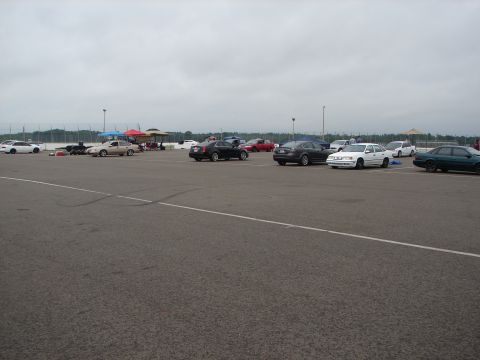 1992 Ford Taurus - A variety of vehicles are parked in a lot, possibly at a car show or event, under an overcast sky.
