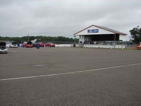 1992 Ford Taurus - Several cars are parked on a paved area, possibly a racetrack, with a covered structure in the background.