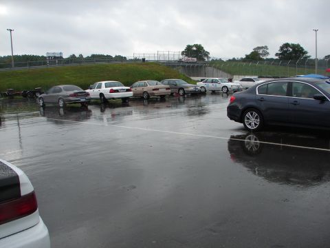 1992 Ford Taurus - Several cars are parked on a wet track surface under an overcast sky.