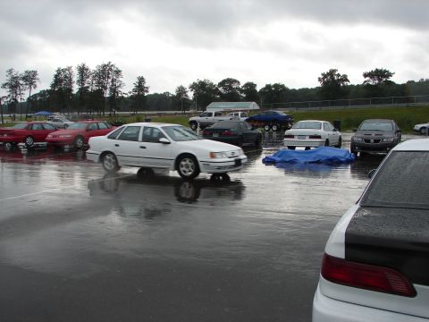 1992 Ford Taurus - A white 1992 Ford Taurus sedan is parked in a lot with other vehicles under a cloudy sky.