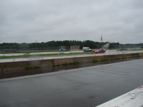 1992 Ford Taurus - A red car and a white van are on a wet race track with trees and a fence in the background.