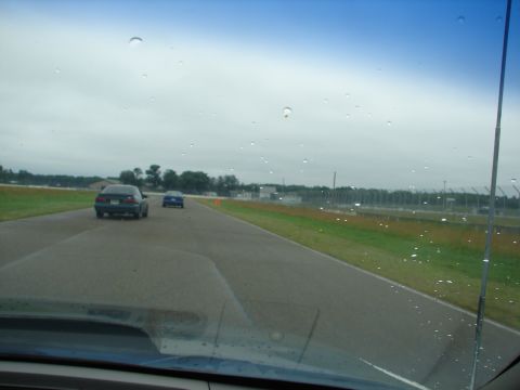 1992 Ford Taurus - Two cars are on a paved track with grass and fencing visible on the sides under a cloudy sky.