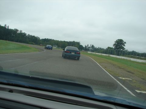 1992 Ford Taurus - A dark sedan drives on a race track with other cars visible in the distance under a cloudy sky.