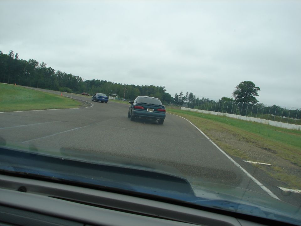 Dark sedan from rear on a race track, cloudy day