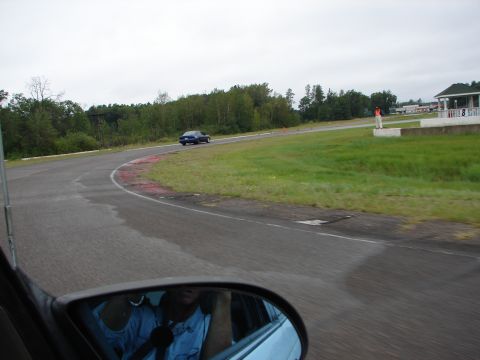 1992 Ford Taurus - A blue sedan drives on a race track under an overcast sky, with trees lining the course.