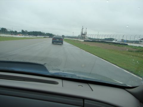 1992 Ford Taurus - A dark sedan navigates a wet racetrack under an overcast sky.
