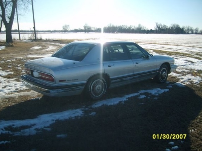 Silver sedan with chrome trim parked on dirt and snow. Rear view shows taillights and trunk
