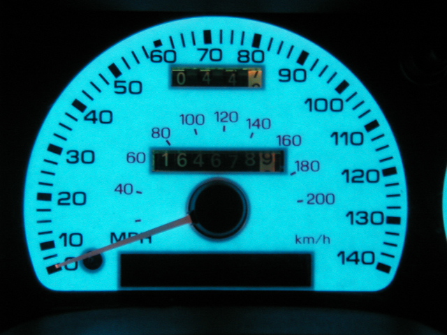 Backlit speedometer reading to 140 mph, odometer 164678, glowing blue-green at night