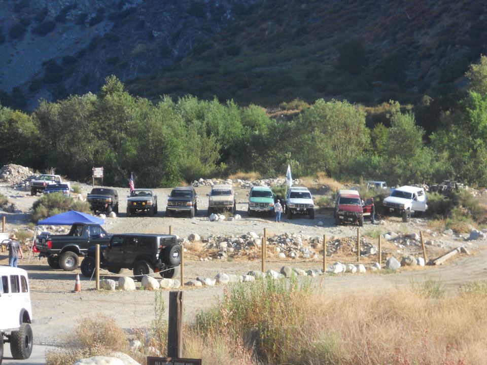 Several SUVs and trucks parked in a dirt lot with trees and a mountain in the background