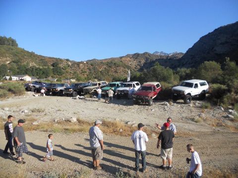 1986 Ford Bronco - Several SUVs and trucks are gathered in a dusty, outdoor area with mountains in the background.