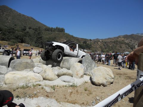 1986 Ford Bronco - A modified off-road vehicle navigates a challenging rock obstacle course with spectators gathered around.