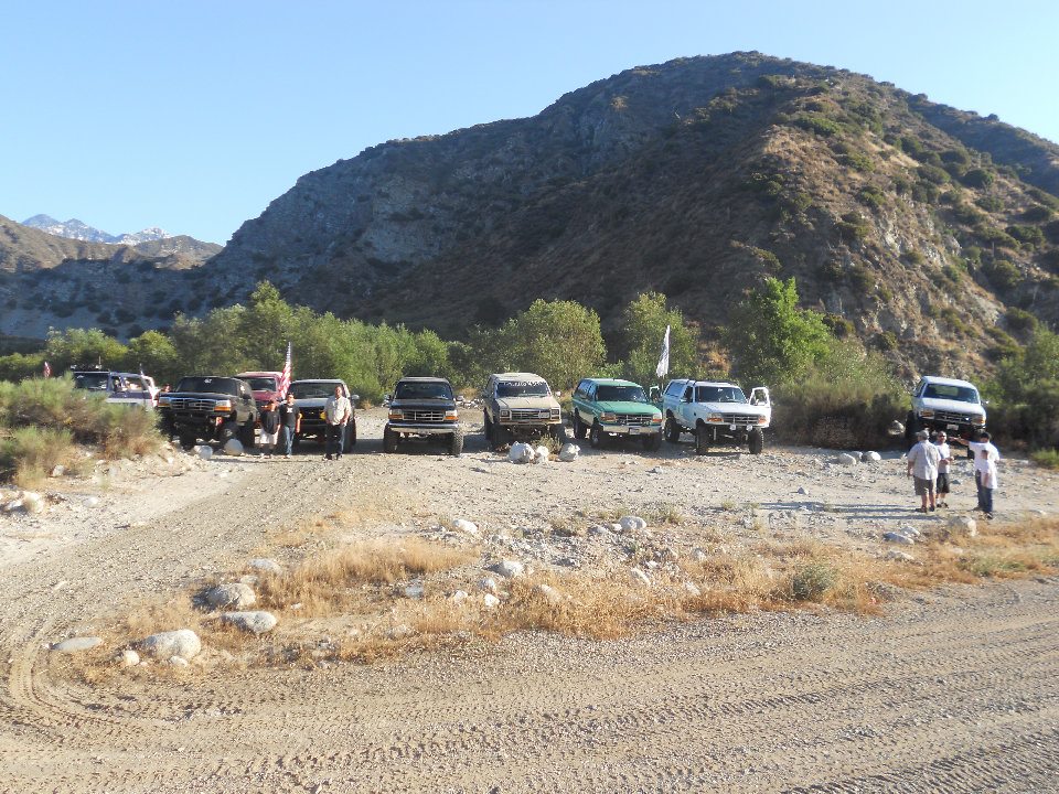 Several off-road SUVs and trucks parked on a dirt road with mountains in the background