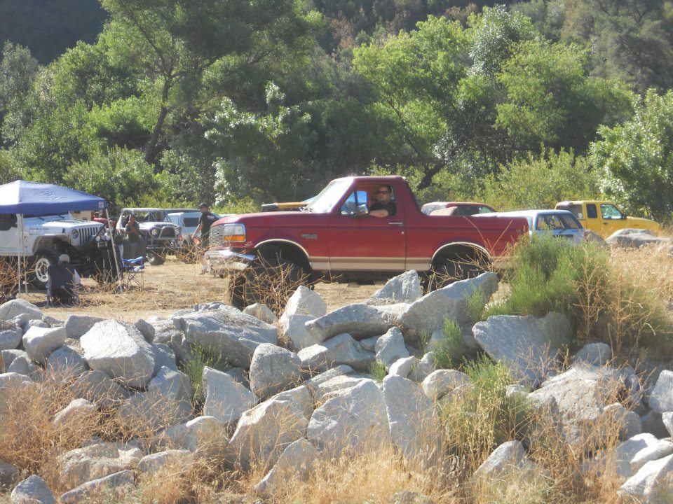 Red Ford Bronco with lifted suspension and tan stripe, parked on rocky terrain
