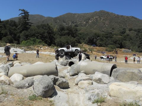 1986 Ford Bronco - Off-road vehicles navigate a rocky obstacle course with large concrete pipes.