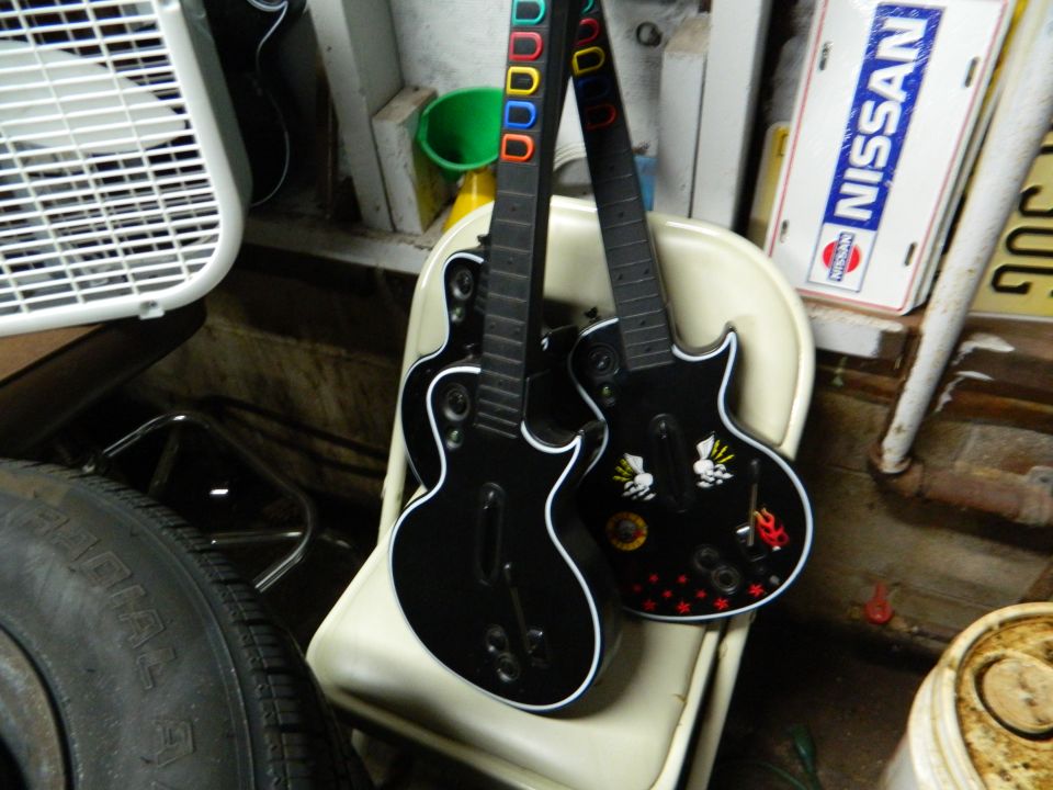 Two black toy guitars leaning on a chair, with a fan and a Nissan sign in the background