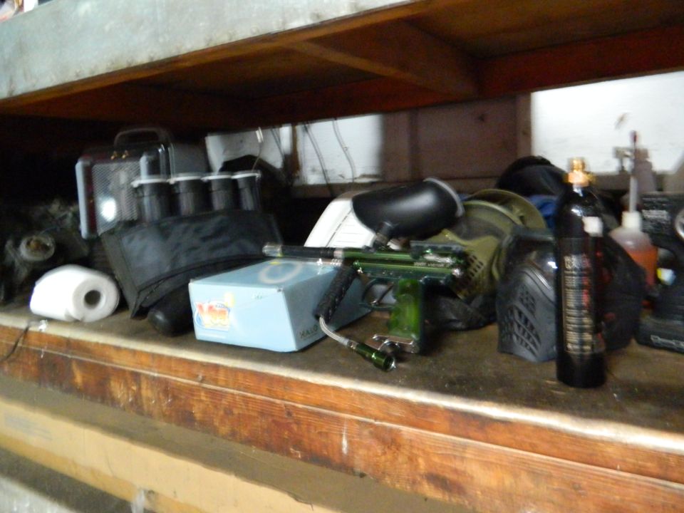 Paintball gun, mask, and air tank on a wooden shelf with other items