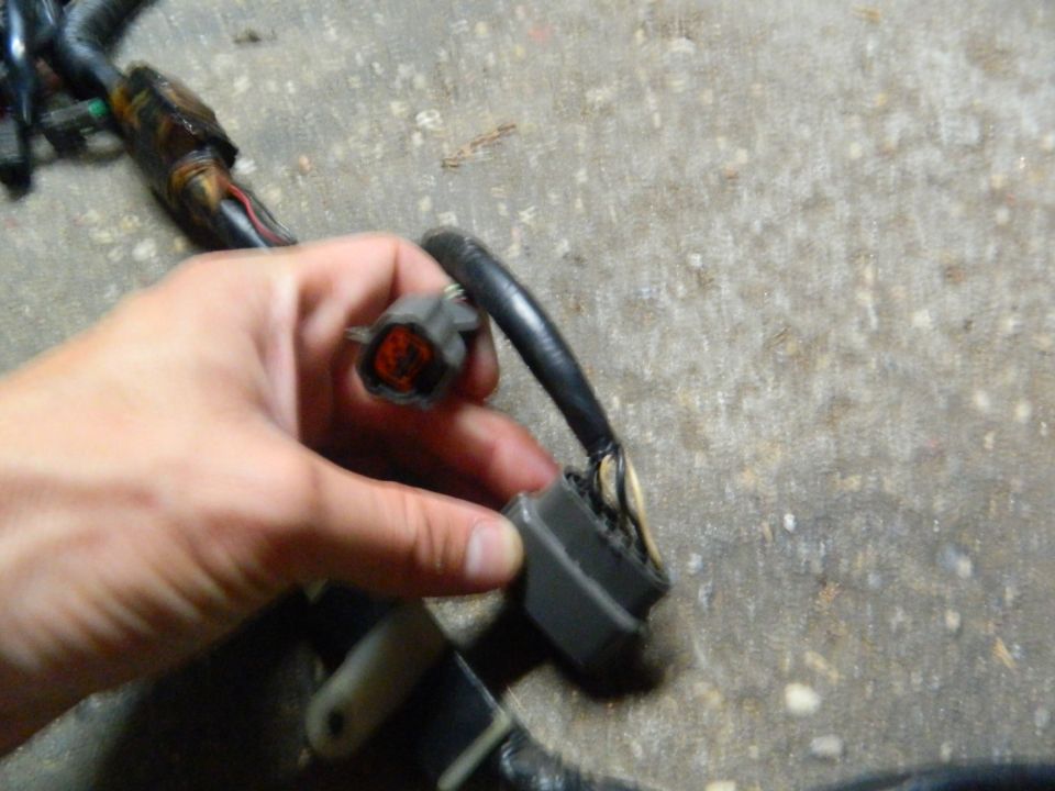 Hand holding a gray electrical connector from a wiring harness