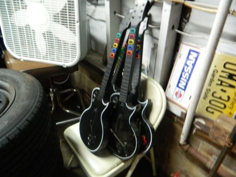 1995 Honda Civic - Several video game guitars are stored in a cluttered area with a fan, spare tire, and various signs on the wall.