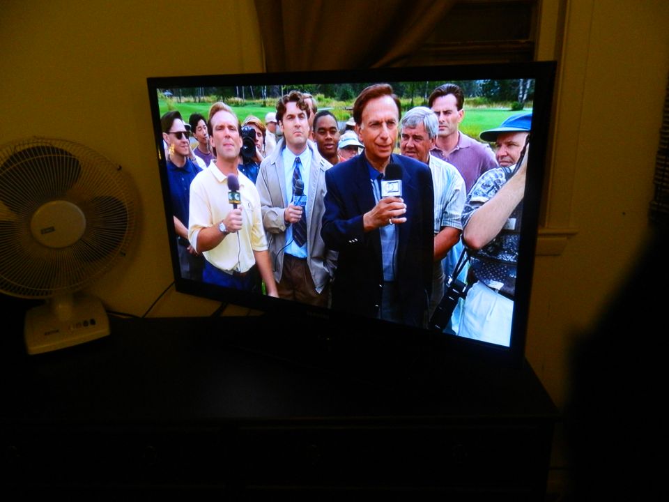 TV screen shows a news reporter interviewing people on a golf course