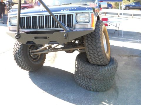 1986 Ford Bronco - A modified Jeep Cherokee XJ is shown with its front passenger tire resting on a stack of two other tires.