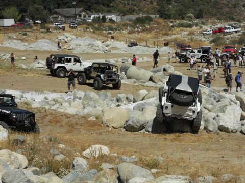 1986 Ford Bronco - Multiple Jeep Wranglers tackle a challenging off-road course with large rocks and uneven terrain.