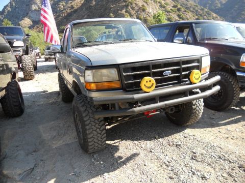 1986 Ford Bronco - Modified gray Ford Bronco parked outdoors with other vehicles. American flag flies from antenna.