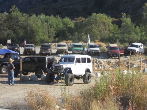 1986 Ford Bronco - A collection of off-road vehicles are gathered in a dusty lot, with a modified white wagon prominently displayed.
