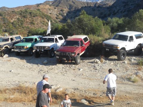 1986 Ford Bronco - Several Ford Broncos are parked on a dirt trail with mountains in the background.