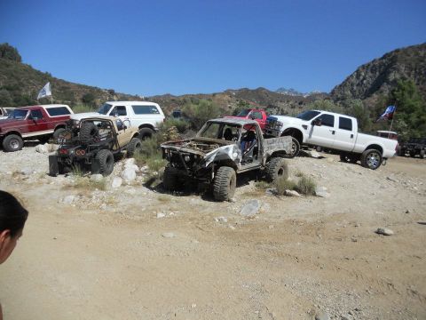 1986 Ford Bronco - A collection of modified trucks and SUVs are gathered on a dusty, outdoor terrain.