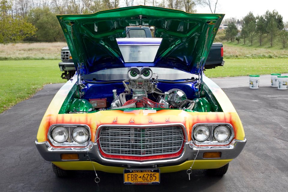 Front view of a heavily modified car with its hood open, showing a large engine. It has a custom paint job and a New York license plate reading FBR-6285