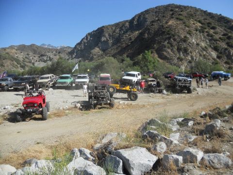 1986 Ford Bronco - Several off-road vehicles are gathered in a scenic, mountainous area under a clear blue sky.
