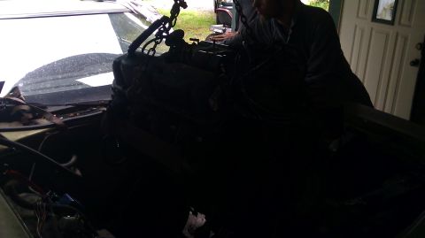 1973 Ford Torino - An engine is being lowered into a vehicle, possibly for a motor rebuild. The exact make and model are unclear.