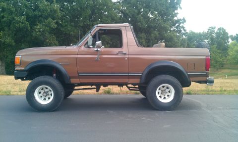 1987 Ford Bronco - This lifted 1987 Ford Bronco is shown from a side profile against a backdrop of trees.