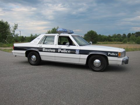 1991 Ford LTD Crown Victoria - A white 1991 Ford Crown Victoria LTD police car with "Boston Police" text and a light bar is parked on an asphalt surface.