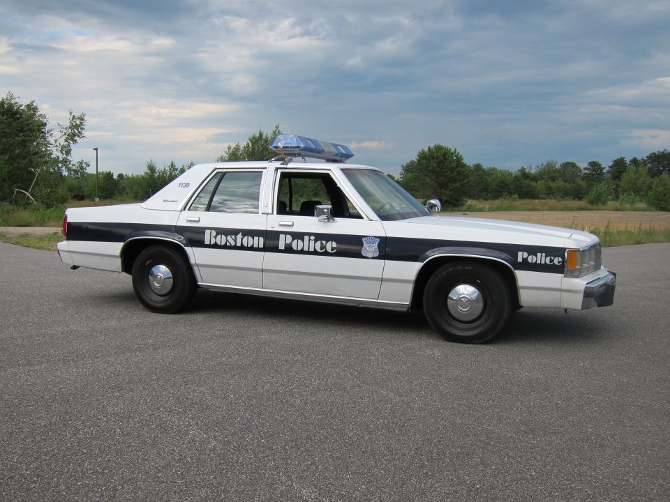 White 1991 Ford Crown Victoria LTD police car with black stripe and "Boston Police" text, parked on asphalt