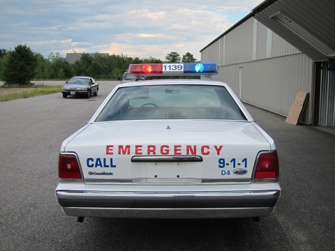 1991 Ford LTD Crown Victoria - Rear view of a 1991 Ford Crown Victoria LTD police car with emergency lights and text on the trunk.