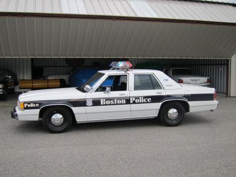 1991 Ford LTD Crown Victoria - Side view of a 1991 Ford Crown Victoria LTD police car parked in front of an open garage.