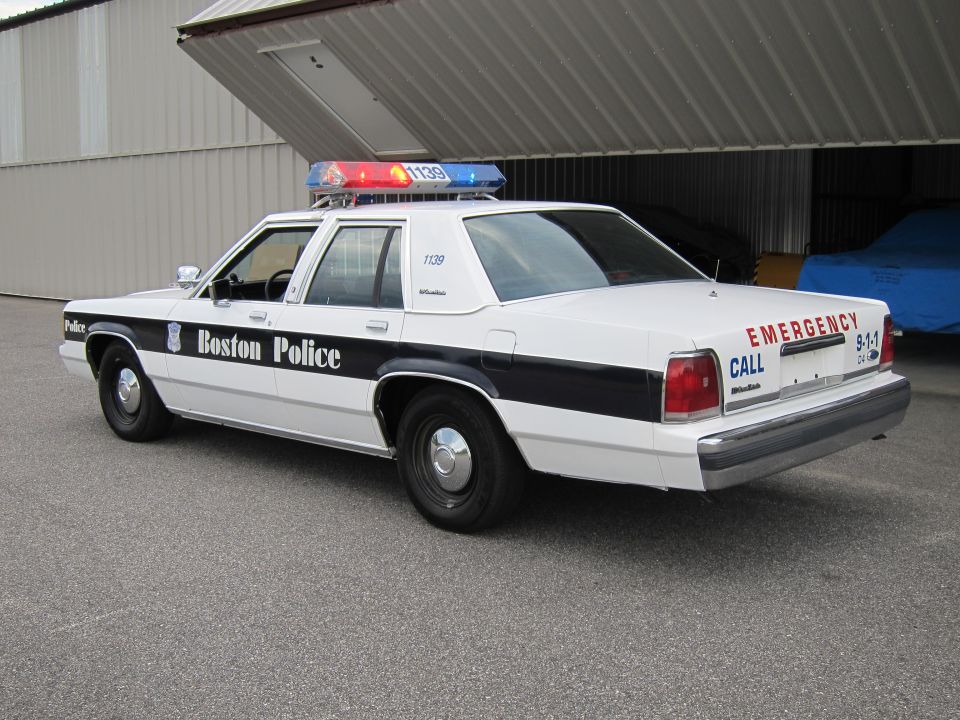 White police car with 'Boston Police' on the side and 'EMERGENCY CALL 9-1-1' on the back