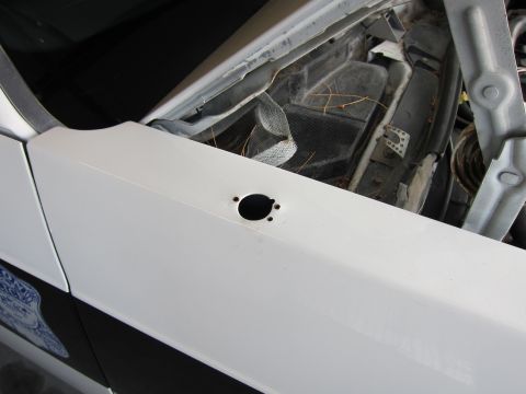 1991 Ford LTD Crown Victoria - A white police car fender shows a hole and partial badge, suggesting a 1991 Ford Crown Victoria LTD.